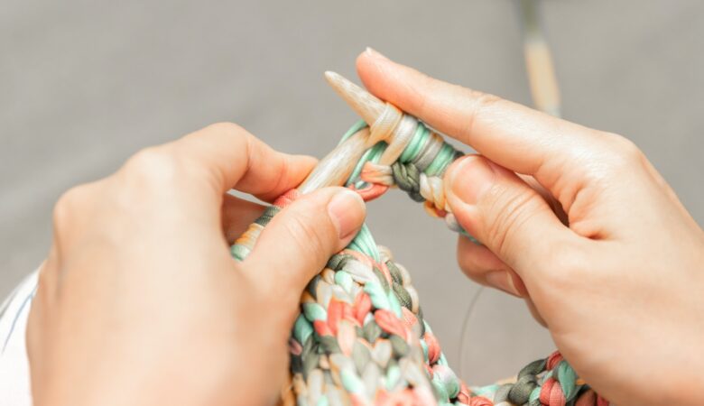 close up a persons hands knitting.